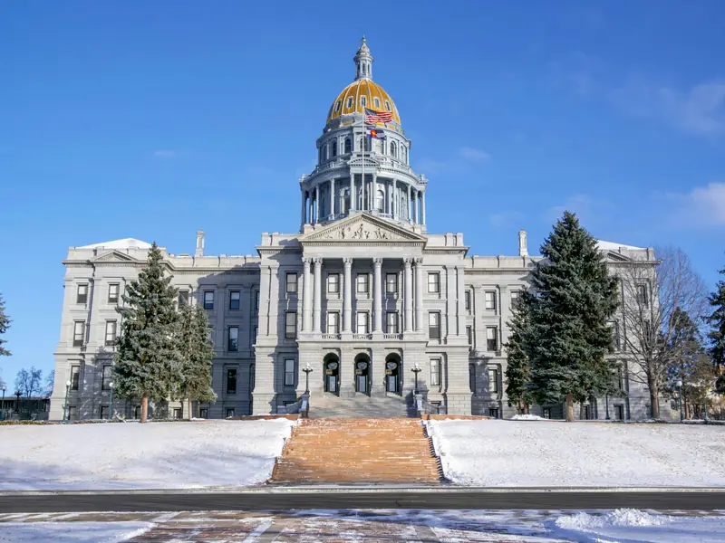 The Colorado State Capitol in Denver, its gold dome against a blue sky, with snow on the lawns.