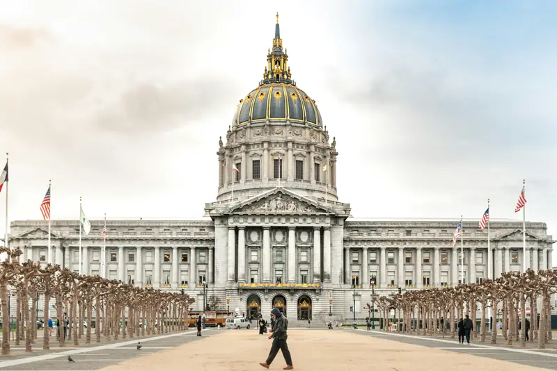 San Francisco City Hall's dome in daylight, with people crossing the plaza in front.
