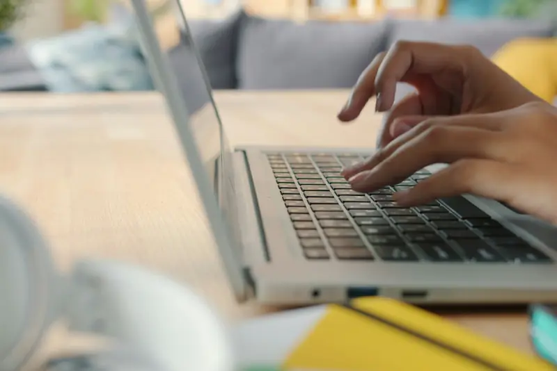 Hands typing on a laptop at a sunny desk.